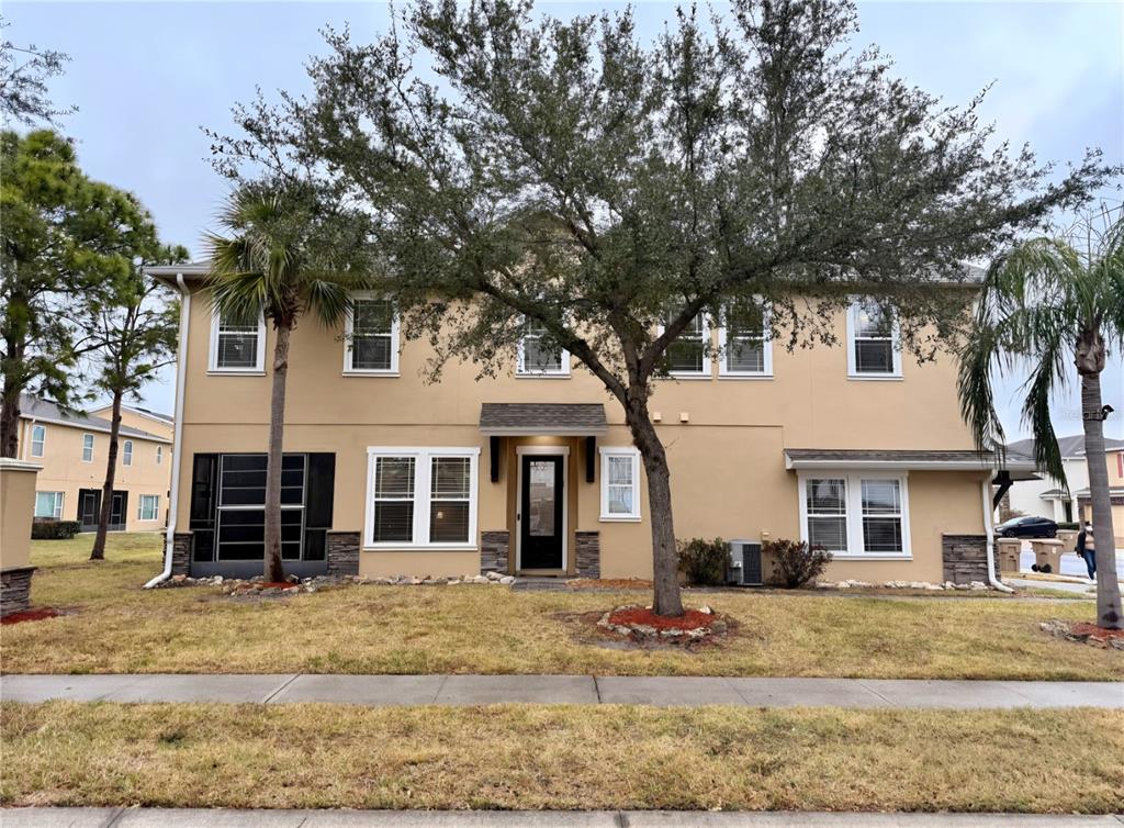 A two-story tan stucco townhouse with a dark front door and a large front tree — 1200 TETON DRIVE, KISSIMMEE, FL