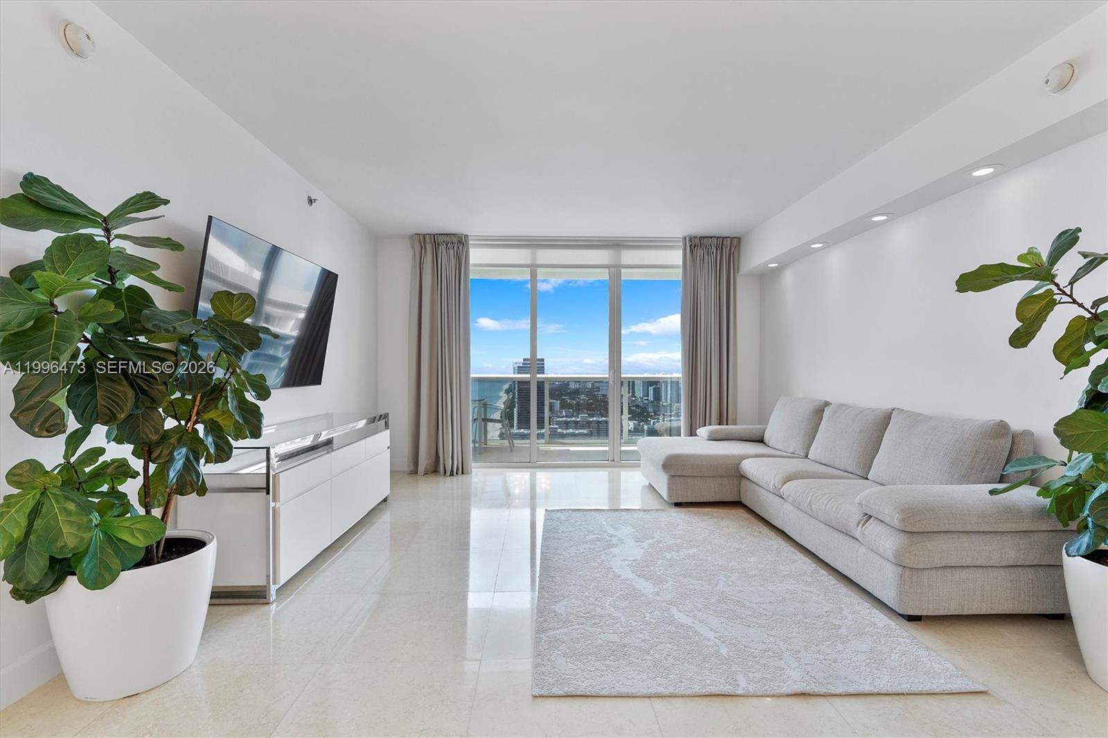 A modern living room features a grey sectional sofa, white media console, and floor-to-ceiling windows — 1830 S Ocean Dr # 4503, Hallandale Beach FL 33009, HALLANDALE BEACH, FL