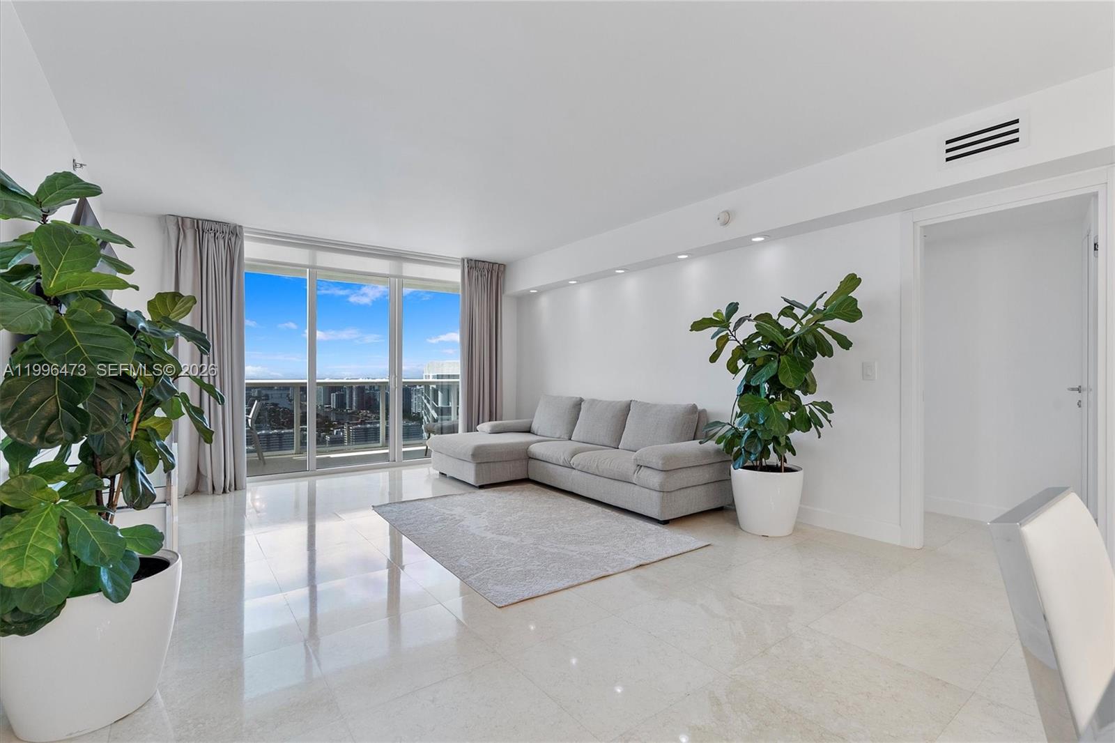 A bright living room features a gray sectional sofa, a rug, and two large potted plants — 1830 S Ocean Dr # 4503, Hallandale Beach FL 33009, HALLANDALE BEACH, FL