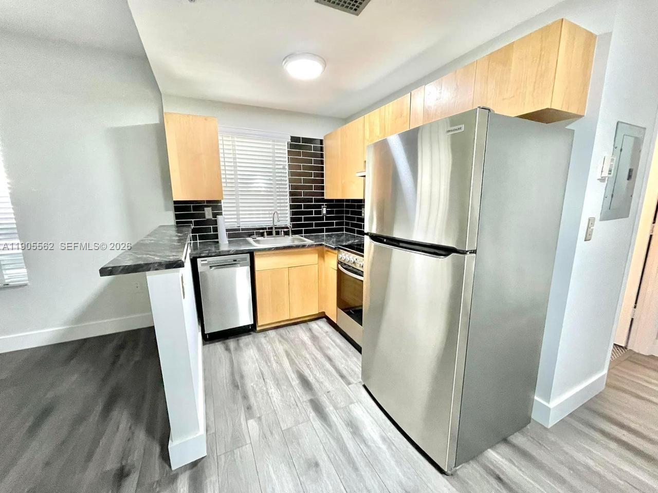 A kitchen features light wood cabinets, stainless steel appliances, and a black tiled backsplash — 1542 Drexel Ave # 107, Miami Beach FL 33139, MIAMI BEACH, FL