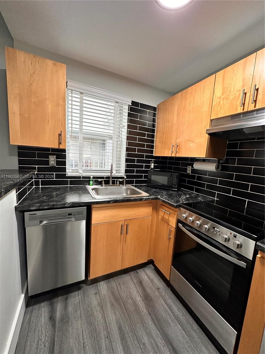 A kitchen features light wood cabinets, black subway tile backsplash, and stainless steel appliances — 1542 Drexel Ave # 107, Miami Beach FL 33139, MIAMI BEACH, FL