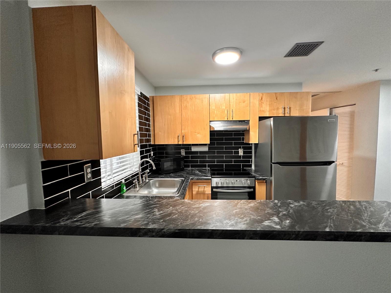 A kitchen features light wood cabinets, black subway tile backsplash, and dark marble-patterned countertops — 1542 Drexel Ave # 107, Miami Beach FL 33139, MIAMI BEACH, FL