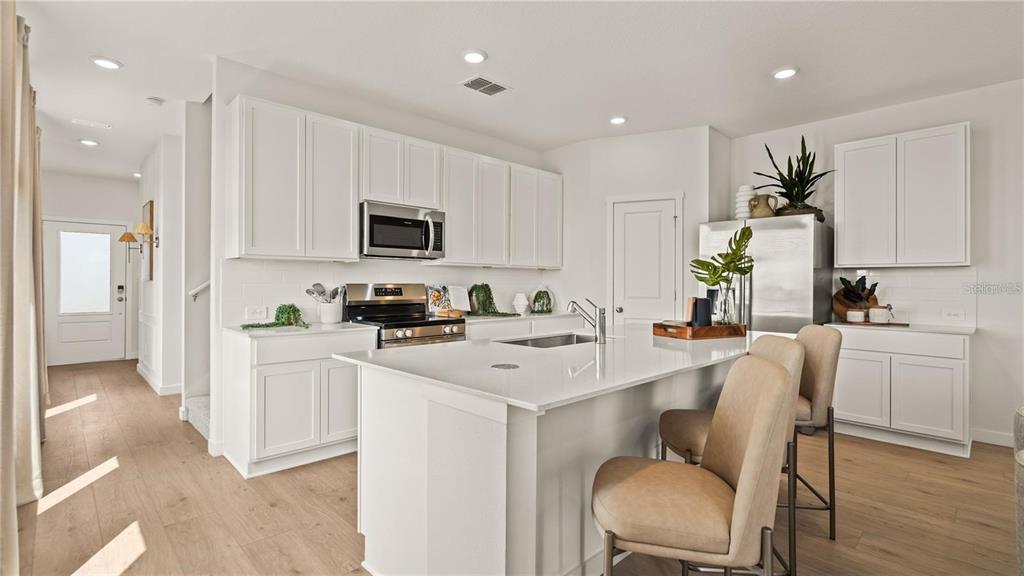 A modern kitchen features white cabinetry, a central island with seating, and light wood flooring — 3035 GRANITE RIDGE AVENUE, MINNEOLA, FL