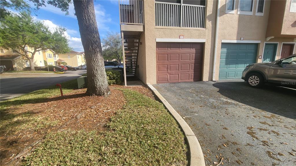 An exterior view shows a multi-story building with two garage doors, a staircase, and a tree — 12024 VILLANOVA DRIVE UNIT 103, ORLANDO, FL
