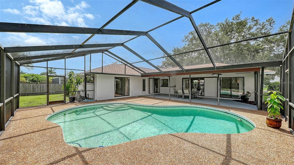 A swimming pool with a pebble deck is enclosed by a screened lanai behind a house — 4736 CHARING CROSS ROAD, SARASOTA, FL
