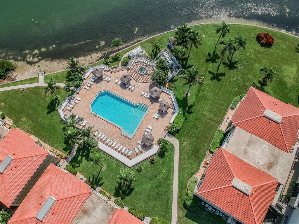 An aerial view shows a swimming pool, patio, and surrounding buildings near a waterfront — 6322 PALMA DEL MAR BOULEVARD S UNIT 1004, ST PETERSBURG, FL