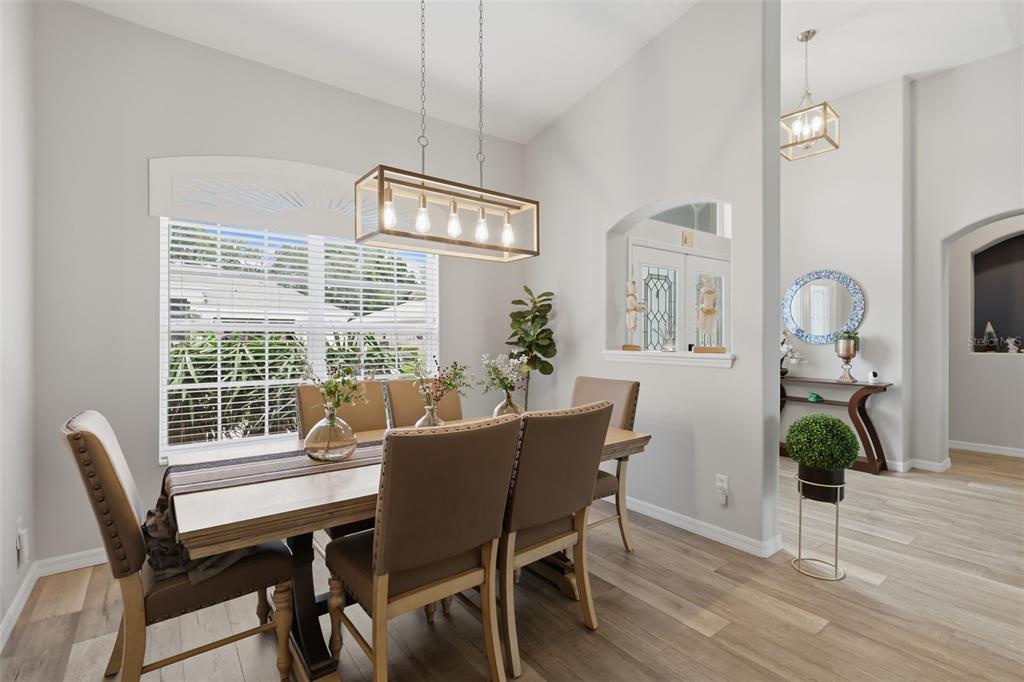 A dining room with a rectangular wooden table, upholstered chairs, and a modern linear chandelier — 5519 AURORA DRIVE, LEESBURG, FL