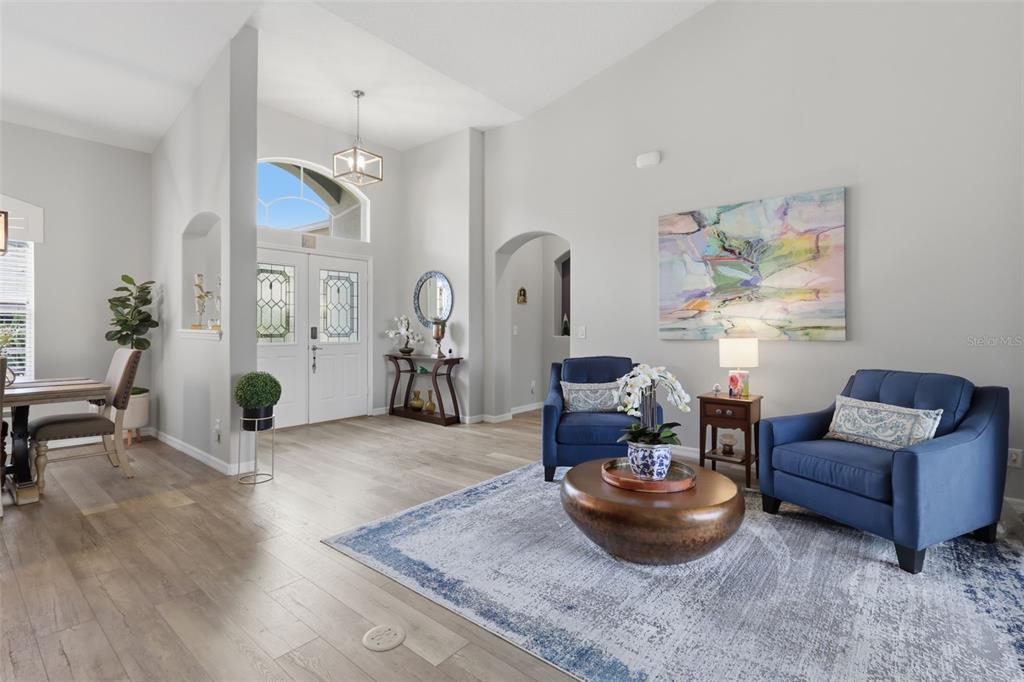 A bright living room features light wood flooring, blue armchairs, and a high vaulted ceiling — 5519 AURORA DRIVE, LEESBURG, FL