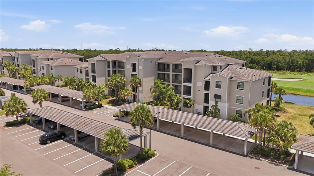 An aerial view shows a multi-story apartment building with covered parking structures and palm trees — 17902 GAWTHROP DRIVE UNIT 305, BRADENTON, FL