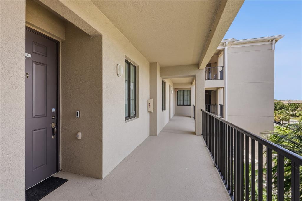 An outdoor apartment corridor features a dark brown door, beige walls, and a metal railing — 17902 GAWTHROP DRIVE UNIT 305, BRADENTON, FL