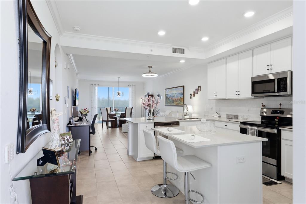 A modern kitchen with white cabinets and a center island opens into a living area — 17902 GAWTHROP DRIVE UNIT 305, BRADENTON, FL