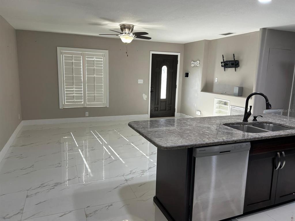 A kitchen with a granite island and stainless steel dishwasher overlooks a room with tile floors — 9724 TOM FOLSOM ROAD, THONOTOSASSA, FL
