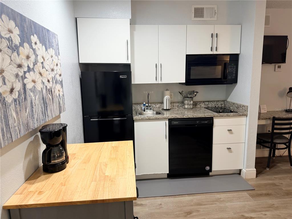 A small kitchen features white cabinets, black appliances, a granite countertop, and a wooden island — 3100 PARKWAY BOULEVARD UNIT 727, KISSIMMEE, FL