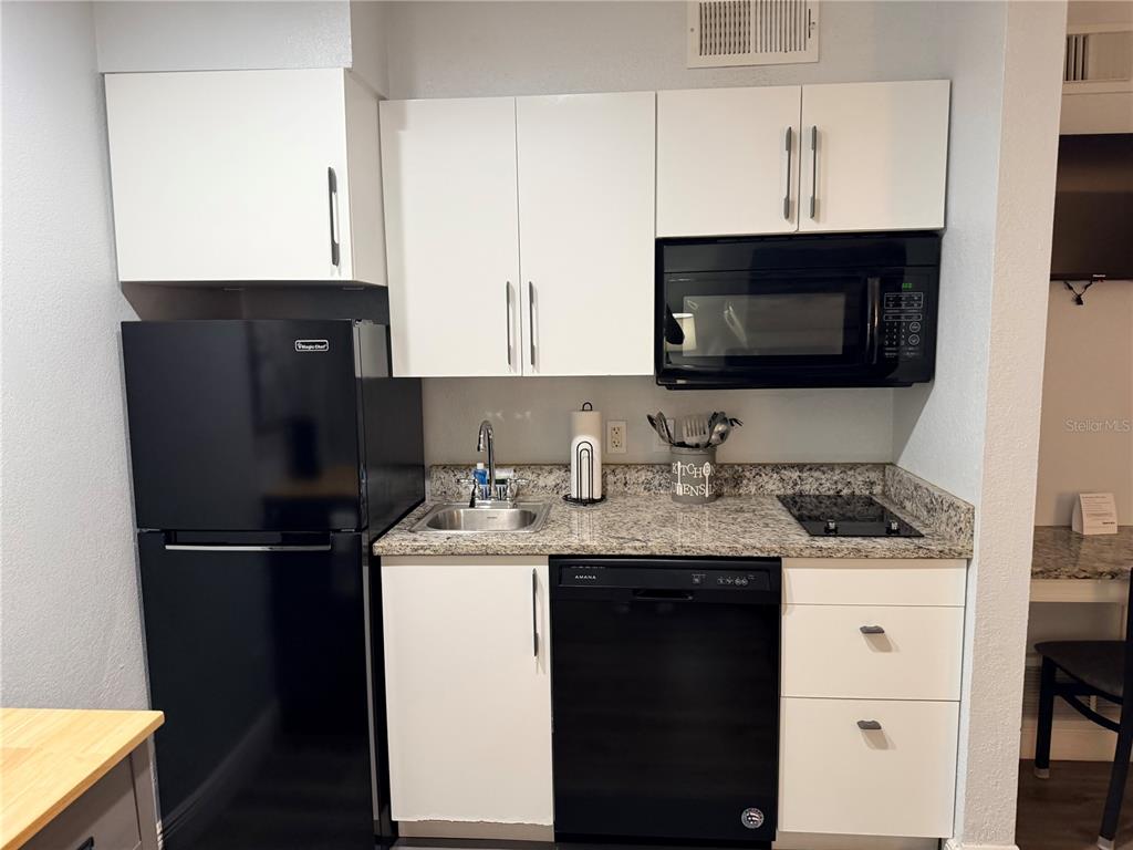 A small kitchen features white cabinets, black appliances, and granite countertops — 3100 PARKWAY BOULEVARD UNIT 727, KISSIMMEE, FL