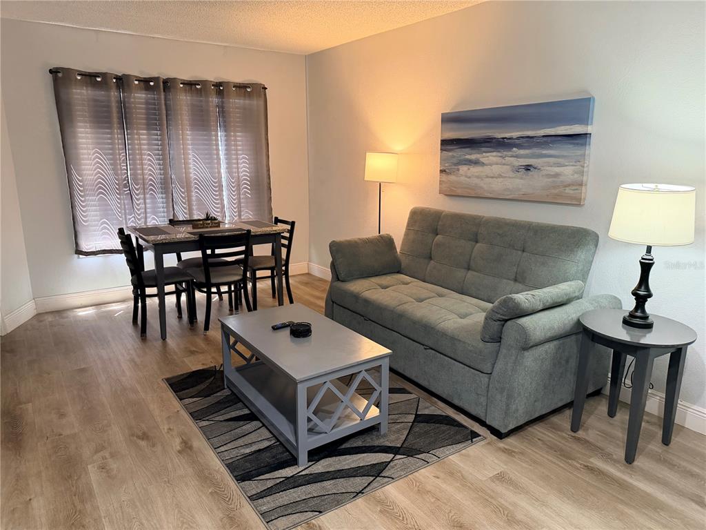 A living and dining area features a grey sofa, coffee table, and a four-person dining set — 3100 PARKWAY BOULEVARD UNIT 727, KISSIMMEE, FL