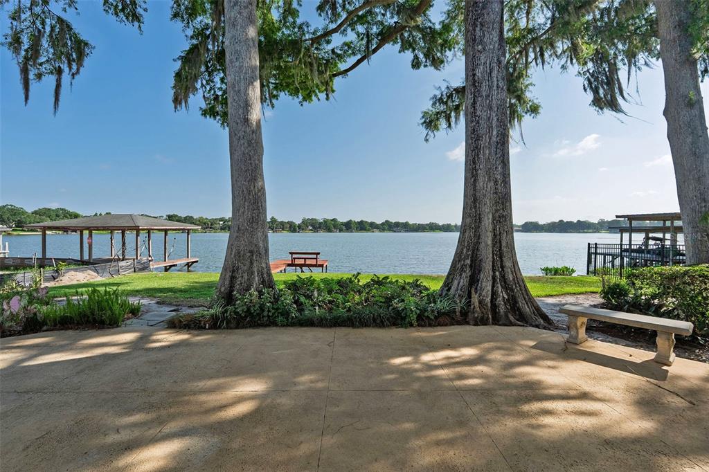 A concrete patio overlooks a lake framed by two large trees and a boat dock — 2655 LAKE SHORE DRIVE, ORLANDO, FL