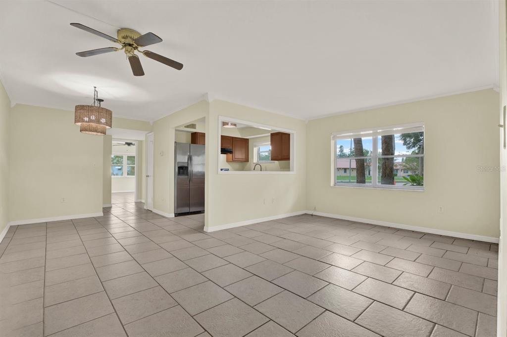 An open-concept dining and living area features light-colored tile flooring and a kitchen pass-through window — 6360 1ST STREET N UNIT 103, ST PETERSBURG, FL