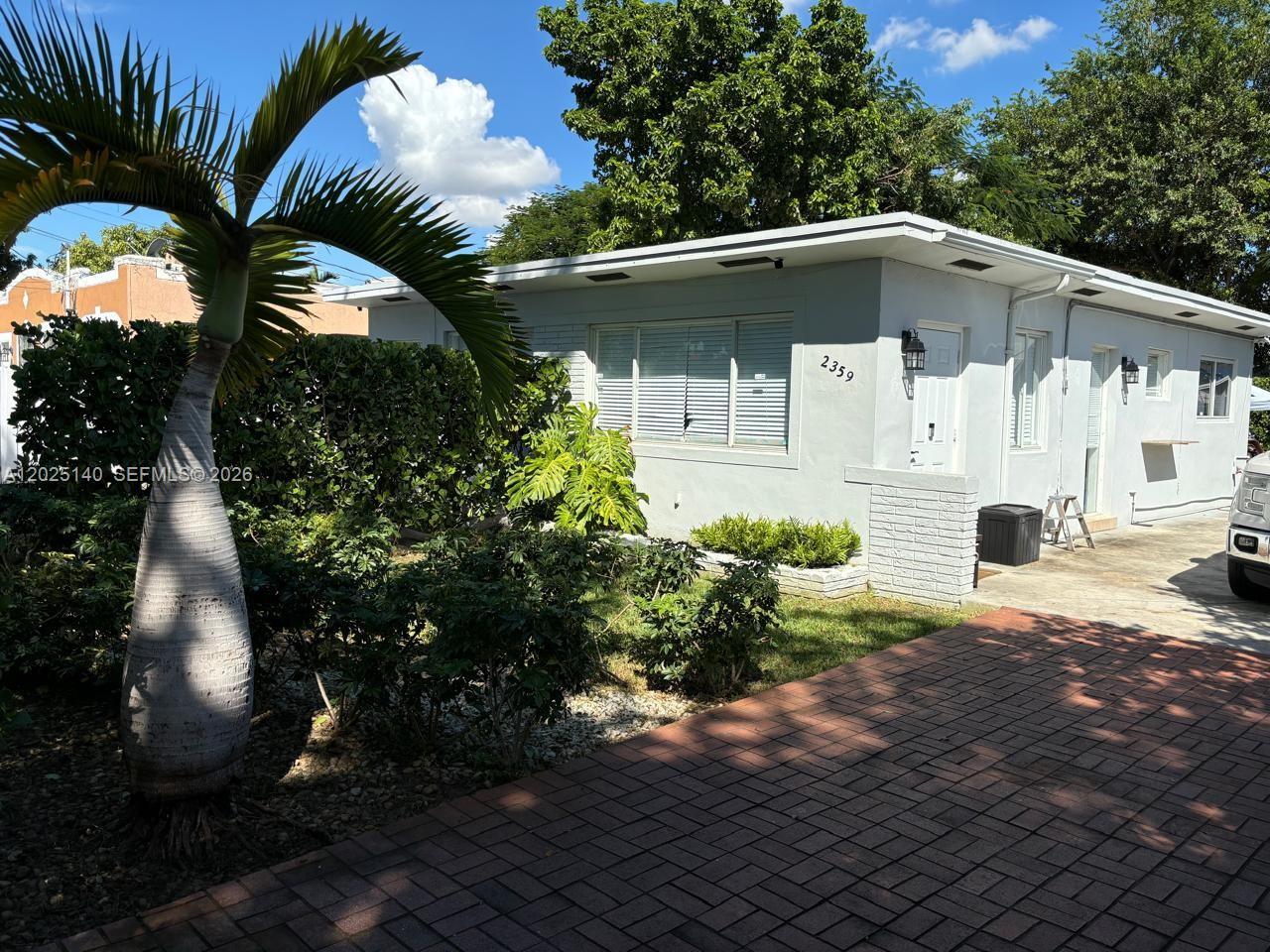 A single-story house with a white exterior, brick driveway, and a palm tree in front — 2359 NW 32nd St, Miami FL 33142, MIAMI, FL
