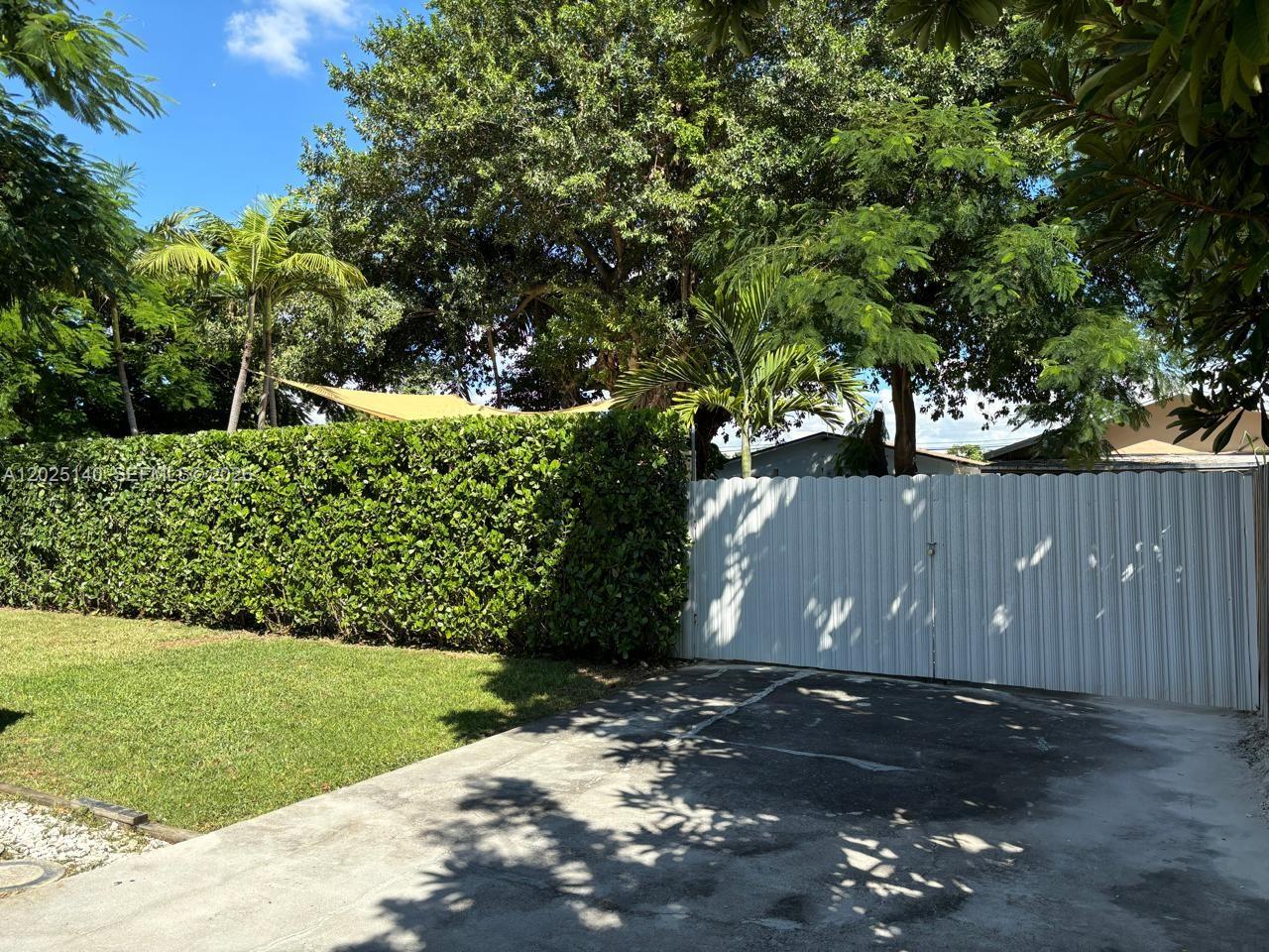 A white metal gate stands beside a tall hedge and a concrete driveway — 2359 NW 32nd St, Miami FL 33142, MIAMI, FL