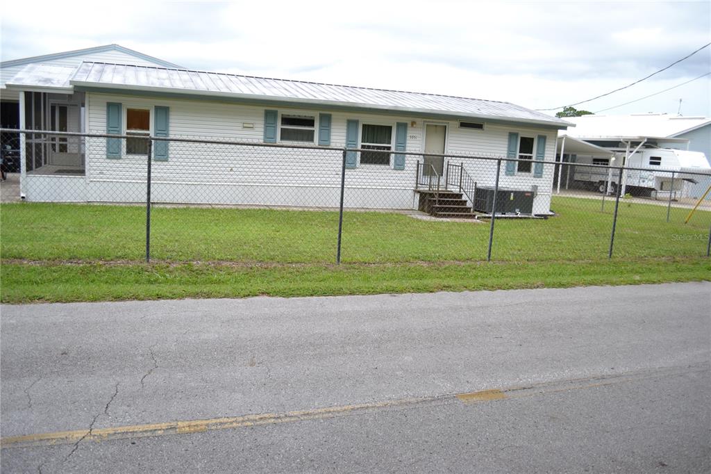 A single-story mobile home with white siding and blue shutters sits behind a chain-link fence — 5951 SE 158TH COURT, OCKLAWAHA, FL