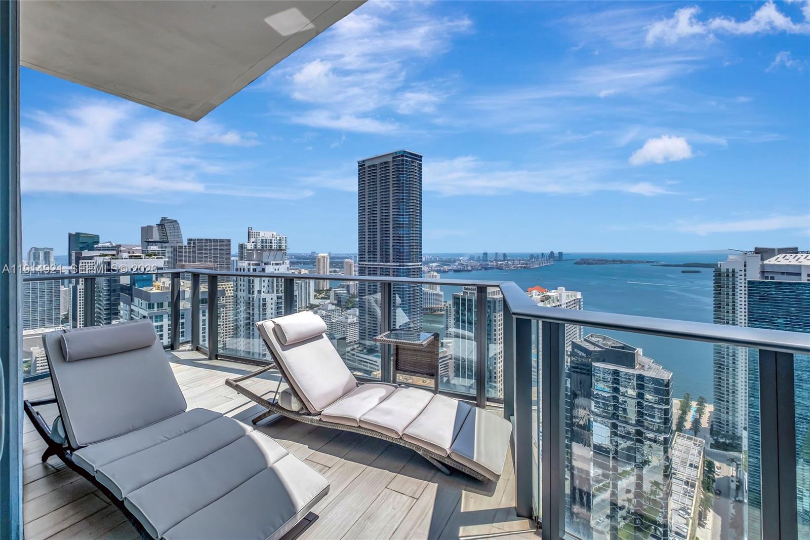 A high-rise balcony features two lounge chairs overlooking a city skyline and the ocean — 1300 S Miami Ave, Miami FL 33130, MIAMI, FL