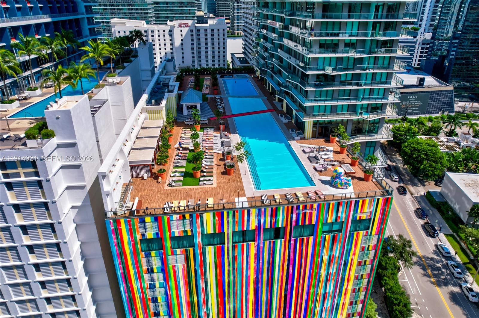 An aerial view shows a colorful building exterior with a rooftop pool and lounge area — 1300 S Miami Ave, Miami FL 33130, MIAMI, FL