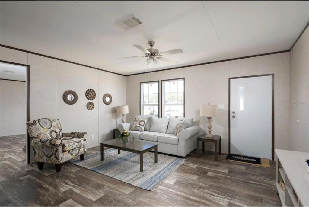 A living room features light-colored walls, wood-look flooring, a sofa, an armchair, and a ceiling fan — 311 CHESSER MONROE ROAD, HAWTHORNE, FL