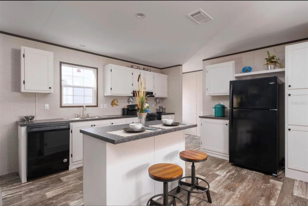 A kitchen features white cabinets, black appliances, a central island with two stools, and wood-look flooring — 311 CHESSER MONROE ROAD, HAWTHORNE, FL