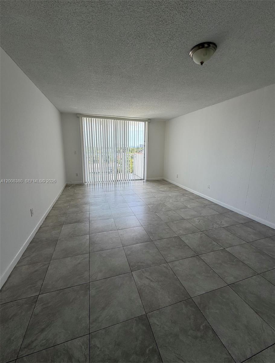 An empty room features gray tile flooring, white walls, and a sliding glass balcony door — NORTH MIAMI, FL