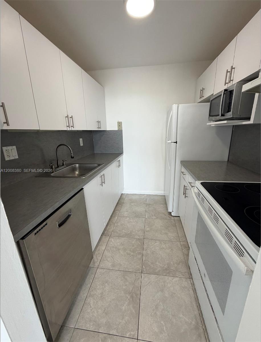 A galley kitchen features white cabinets, stainless steel appliances, and gray countertops — NORTH MIAMI, FL