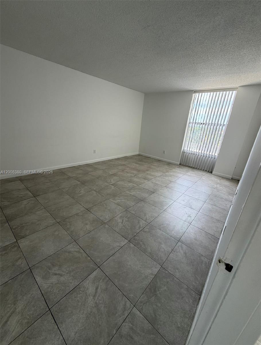An empty room features large gray floor tiles, white walls, and vertical window blinds — NORTH MIAMI, FL