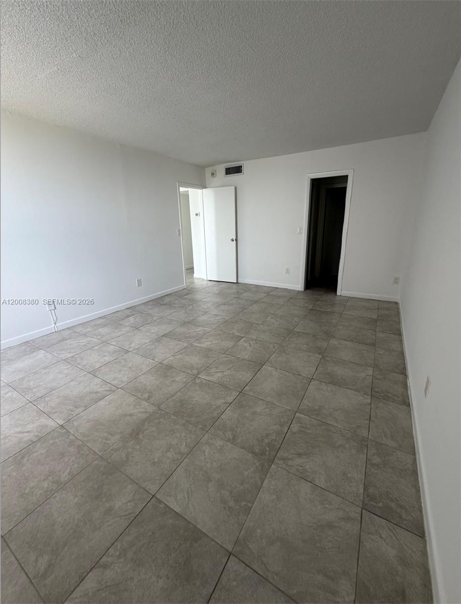 An empty room features white walls, a textured ceiling, and large light-gray floor tiles — NORTH MIAMI, FL