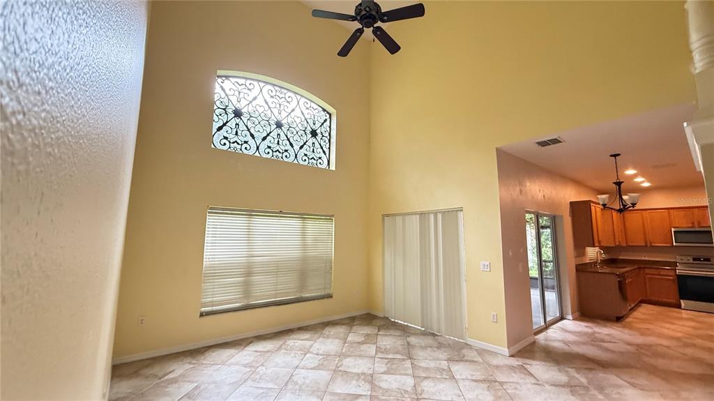 A high-ceilinged living room with tile floors, a ceiling fan, and an adjacent kitchen — 3559 SUNSET ISLES BOULEVARD, KISSIMMEE, FL