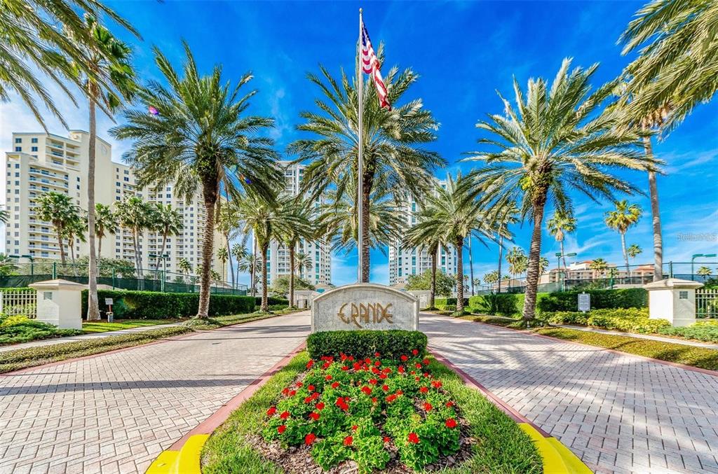 A stone monument sign for Grande stands at the entrance of a palm-lined driveway — 1180 GULF BOULEVARD UNIT 1703, CLEARWATER BEACH, FL