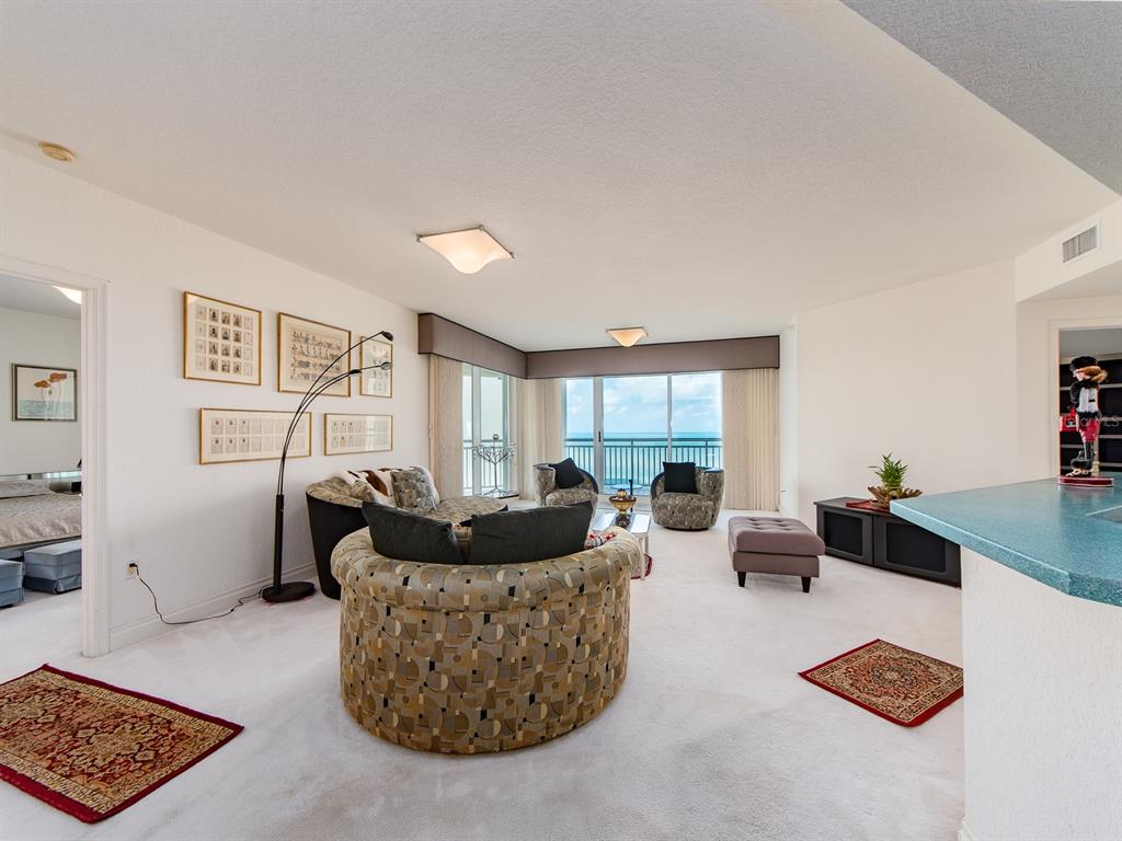 A living room with patterned circular chairs, white carpeting, and a view of the ocean — 1180 GULF BOULEVARD UNIT 1703, CLEARWATER BEACH, FL
