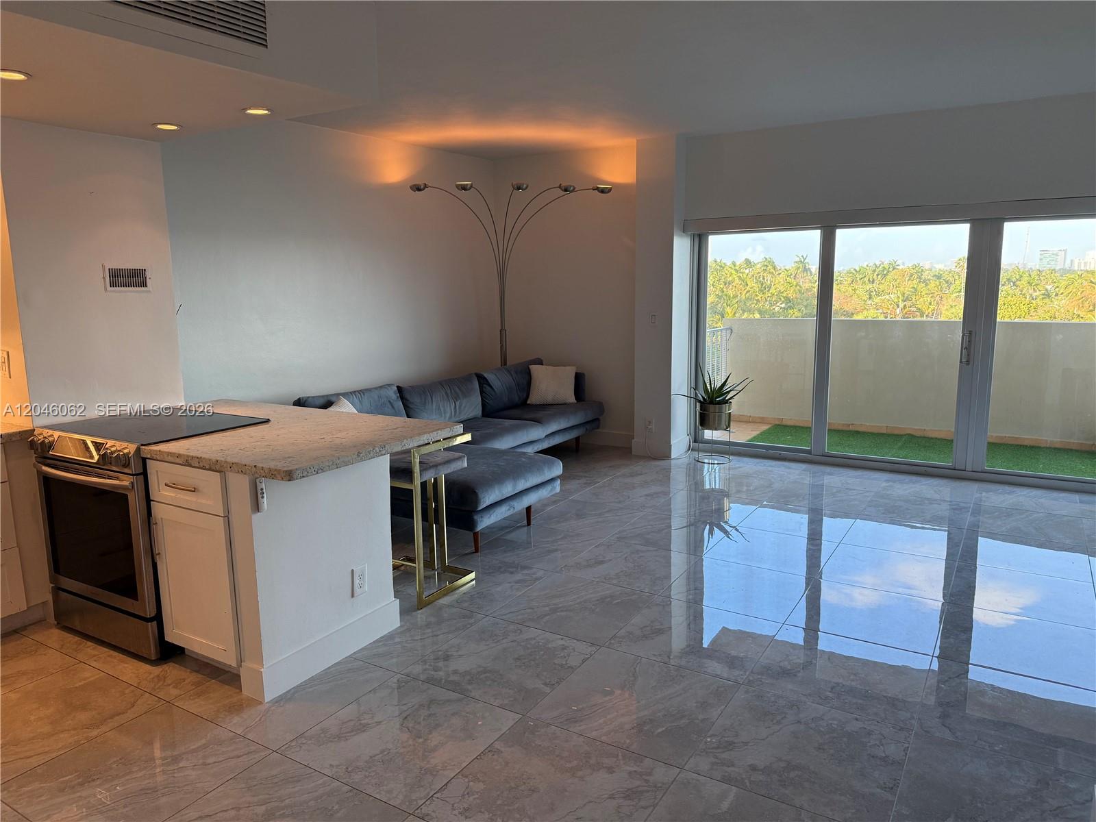 A modern living room features gray tile floors, a velvet sectional, and a balcony view — 880 NE 69th St # 5Q, Miami FL 33138, MIAMI, FL