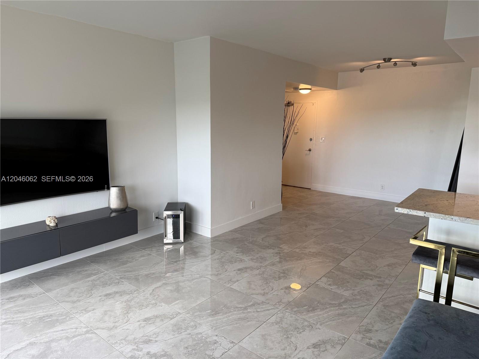 A living room features gray tile flooring, a wall-mounted television, and a breakfast bar — 880 NE 69th St # 5Q, Miami FL 33138, MIAMI, FL