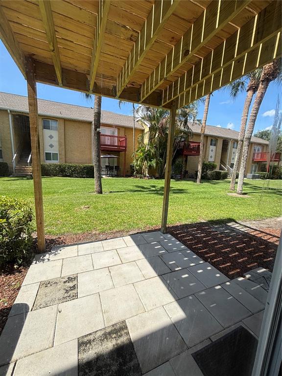 A ground-level patio with stone pavers sits beneath a wooden deck overlooking a grassy courtyard — 1968 TOUCAN WAY UNIT 1404, SARASOTA, FL