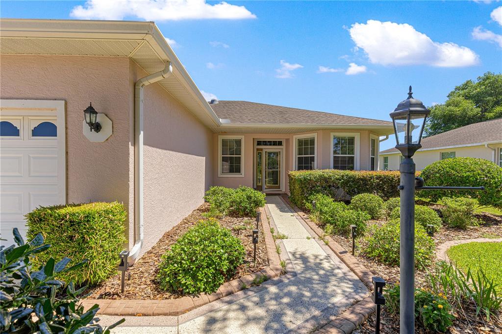 A walkway leads to the front entrance of a house with a beige exterior — 9317 SW 94TH LOOP, OCALA, FL