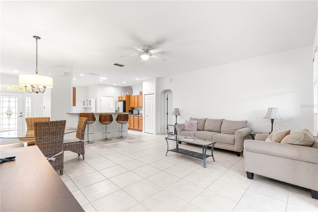 An open-concept living and dining area features tile flooring, a kitchen island, and neutral furniture — 9317 SW 94TH LOOP, OCALA, FL