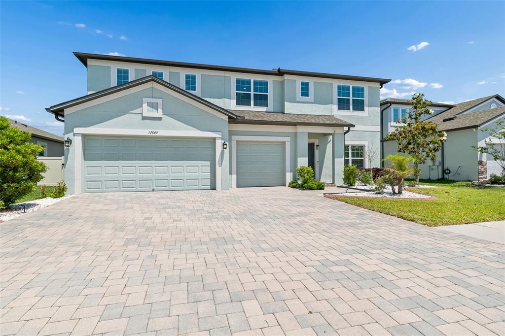 A two-story house with a light green exterior, a paved driveway, and a three-car garage — 17647 CORTES CREEK BOULEVARD, SPRING HILL, FL