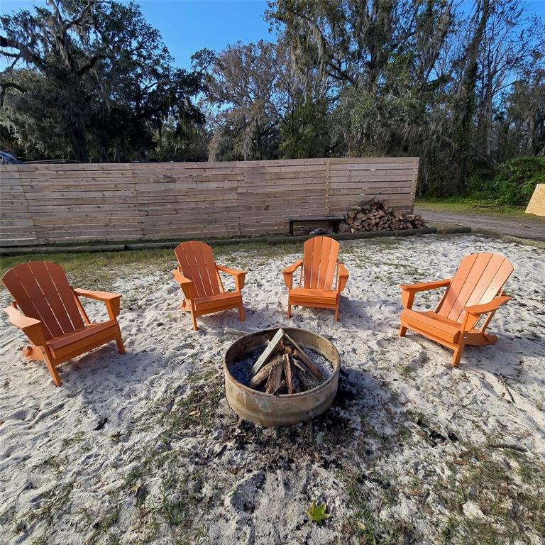 Four orange Adirondack chairs are arranged around a metal fire pit in a sandy yard — 19240 SE HIGHWAY 42, WEIRSDALE, FL