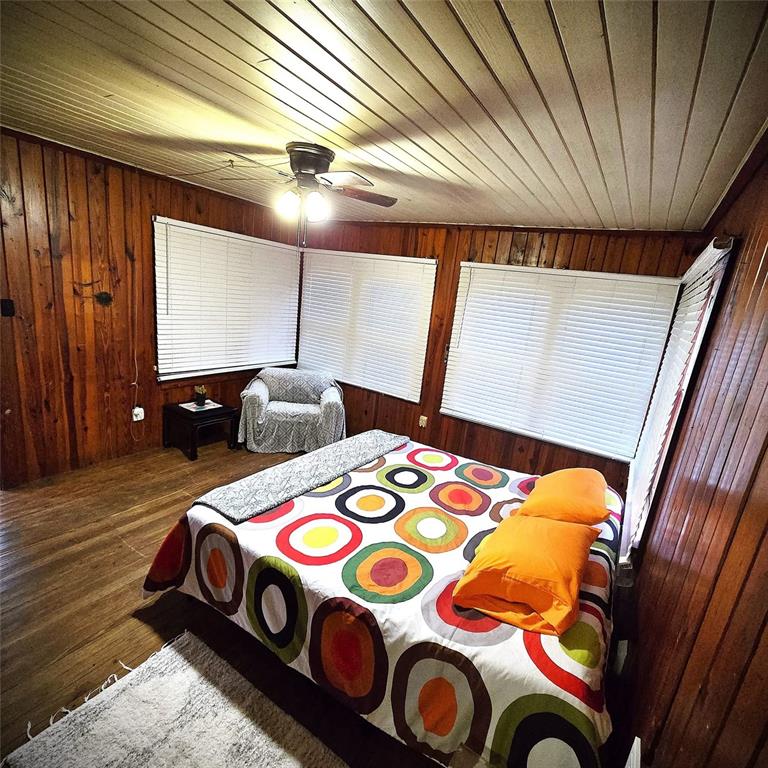 A bedroom features wood-paneled walls, a ceiling fan, and a bed with a colorful pattern — 19240 SE HIGHWAY 42, WEIRSDALE, FL