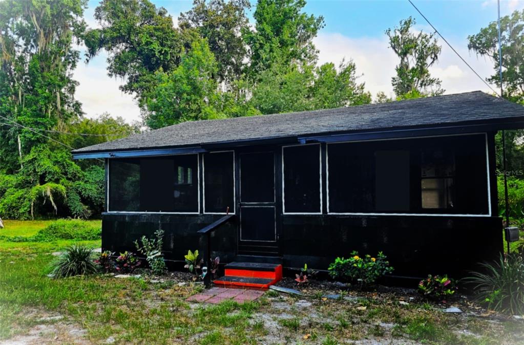 A small, black-painted house with a screened-in porch and red steps sits in a yard — 19240 SE HIGHWAY 42, WEIRSDALE, FL