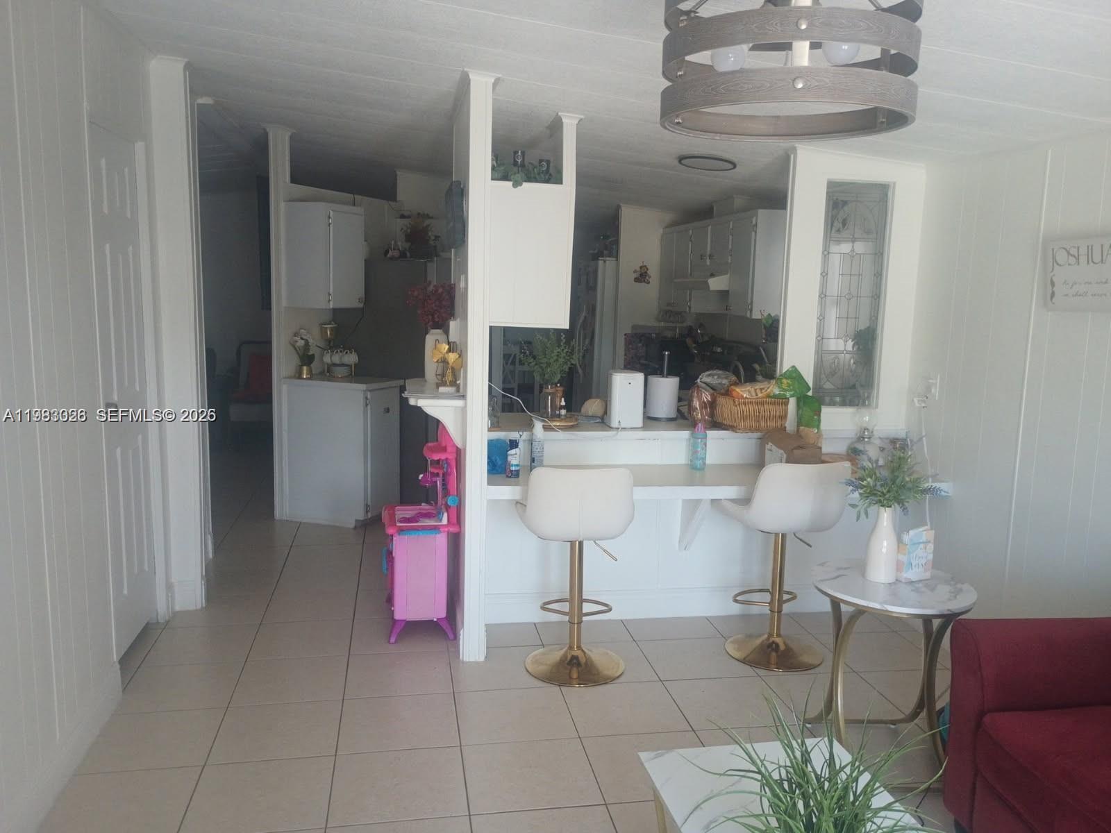 A kitchen with a breakfast bar, white cabinetry, and tile flooring opens into a living area — 3024 SW 51st St, Dania Beach FL 33312, DANIA BEACH, FL