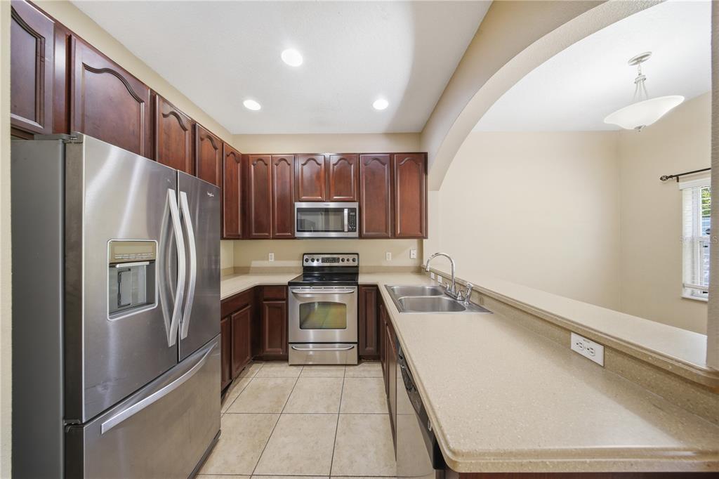 A kitchen with dark wood cabinets, stainless steel appliances, and beige countertops — 10291 PARK COMMONS DRIVE, ORLANDO, FL