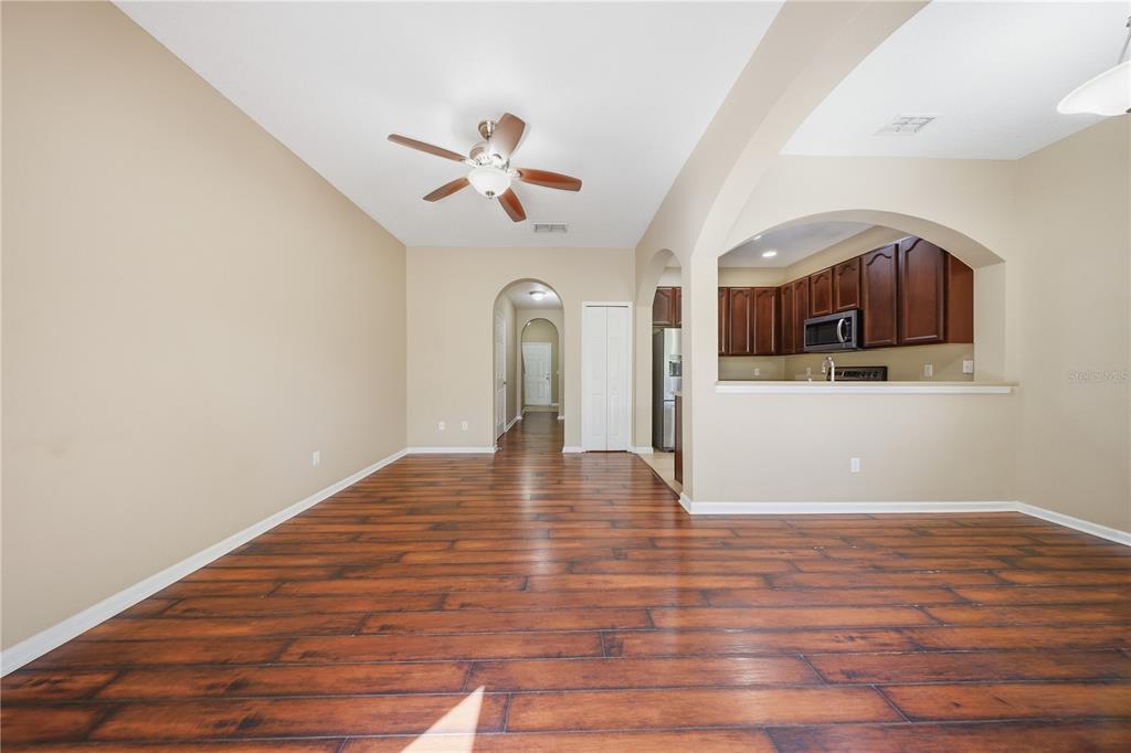 A living room with wood-look flooring leads to an arched opening into the kitchen — 10291 PARK COMMONS DRIVE, ORLANDO, FL