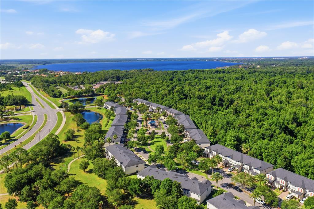 An aerial view shows a multi-building residential complex surrounded by trees near a large lake — 10291 PARK COMMONS DRIVE, ORLANDO, FL