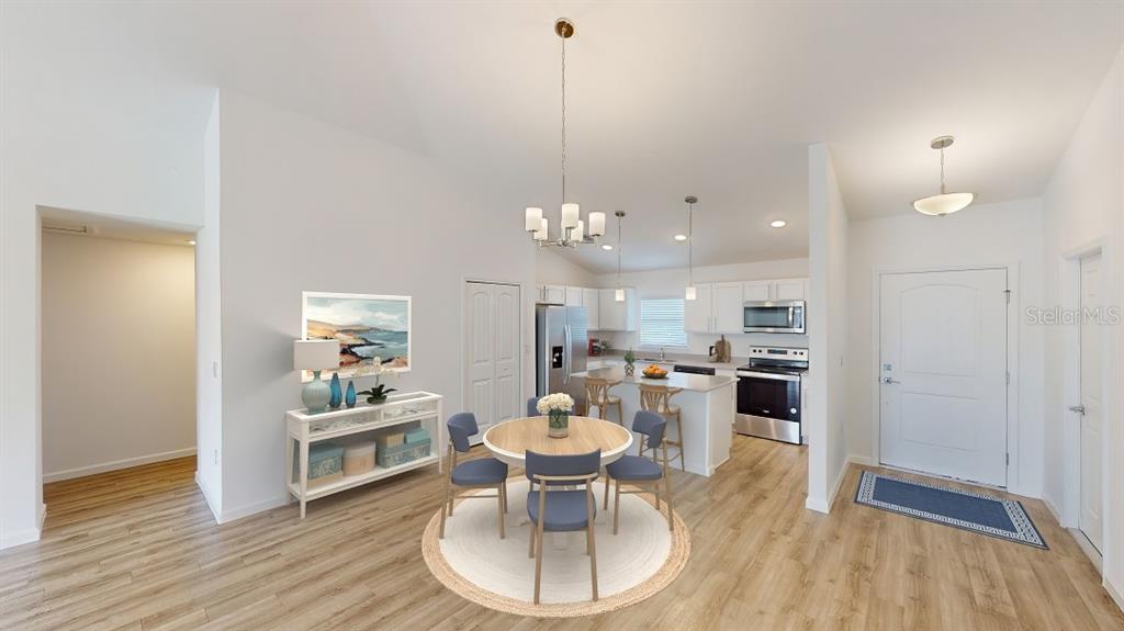 This open-concept kitchen and dining area features light wood flooring, white cabinetry, and a chandelier — 1620 GERANIUM AVENUE, NORTH PORT, FL