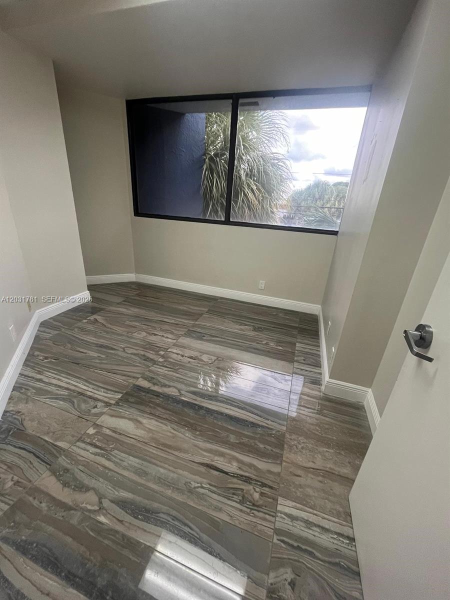 An empty room features large, glossy, marble-patterned floor tiles and a window overlooking palm trees — 6101 W Atlantic Blvd # 208, Margate FL 33063, MARGATE, FL